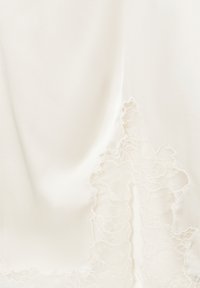 Tissu en satin crème avec une délicate application de dentelle blanche ornée de motifs floraux le long du bord.