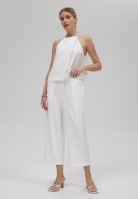 Hvit halter-neck topp med flytende design, kombinert med vide hvite bukser. Glatt stoff og minimalistisk stil med subtil glød.