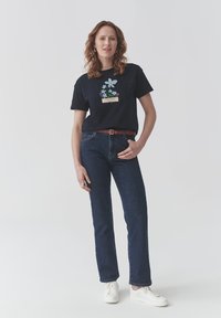 T-shirt en coton marine avec imprimé floral, assortie à un jean en denim foncé. Des baskets blanches et une ceinture marron complètent l'ensemble.