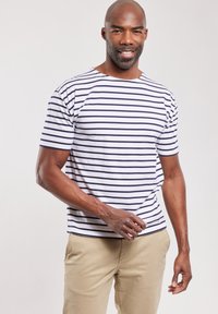 Camiseta de manga corta a rayas, base blanca con rayas azul marino, cuello redondo, material de algodón, corte relajado, combinada con pantalones beige.
