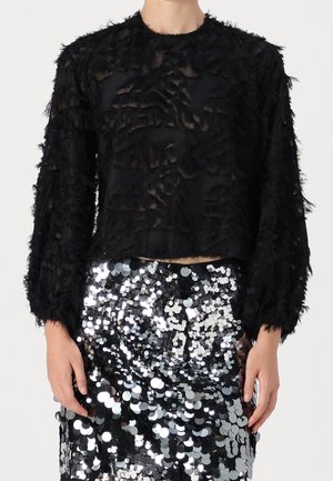 Schwarzes, strukturiertes Langarmshirt mit Fransen, kombiniert mit einem schimmernden silbernen Paillettenen Rock, der einen geschichteten Effekt erzeugt.