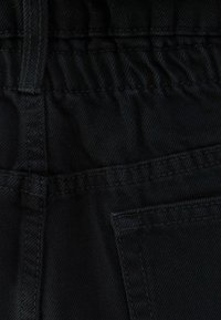 Tejido negro con un acabado texturizado, que presenta una cinturilla elástica y un bolsillo lateral cosido. El material parece duradero y flexible.