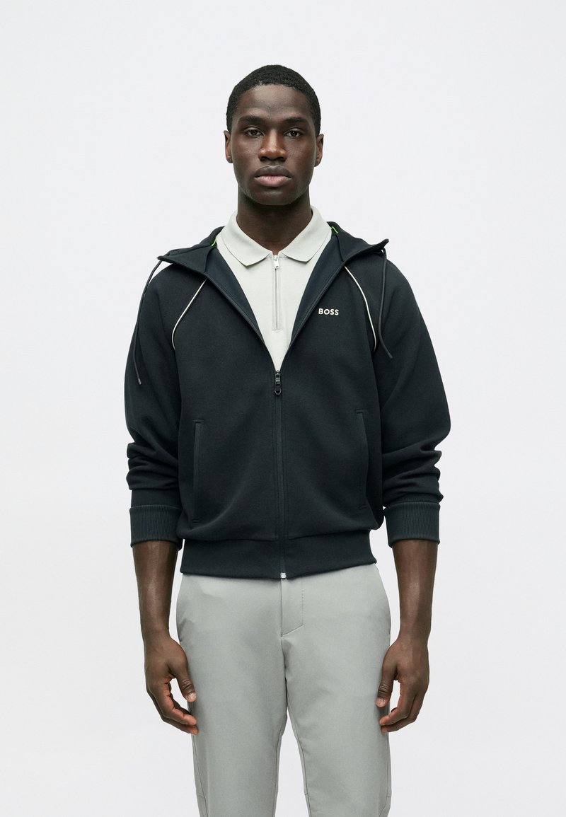 Μαύρο hoodie με φερμουάρ και λευκές γραμμές τόνου, με το λογότυπο "BOSS" στο στήθος, συνδυασμένο με ανοιχτό γκρι πόλο. Ομαλή υφή υφάσματος.