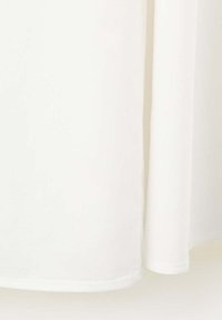Gros plan d’un rideau en tissu blanc suspendu droit avec une ombre subtile le long du pli sur un fond uni.