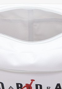 Borsa bianca con zip realizzata in tessuto testurizzato; presenta un logo rosso e testo nero; l'interno mostra una fodera chiara con dettagli di tasca in rete.