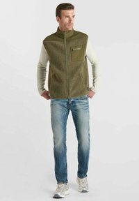 Fleece-Weste in Olivgrün mit Reißverschluss, strukturiertem Körper und einfarbigen Ärmeln. Kombiniert mit hellblauen Jeans und grauen Sneakers.