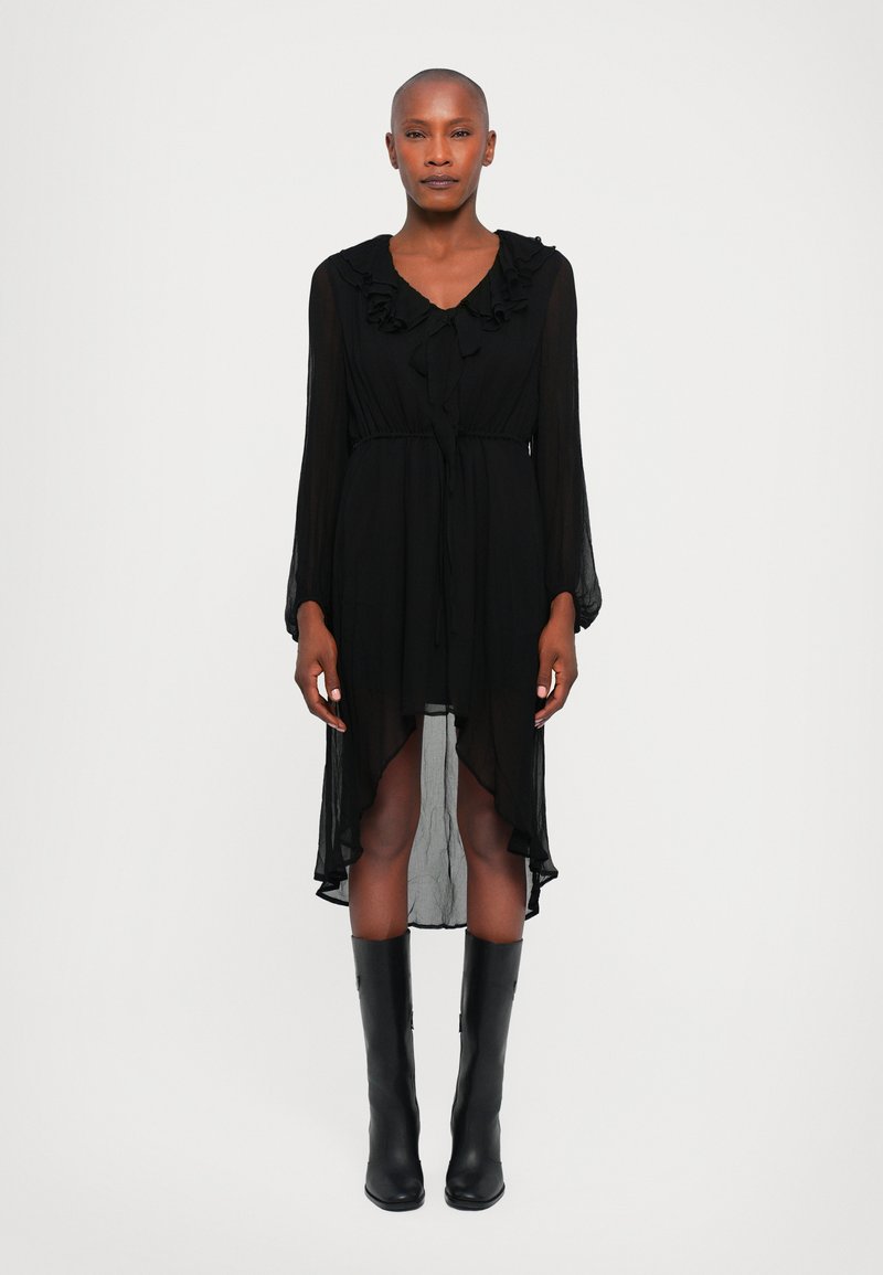 Rochie din chiffon negru cu guler volanat și mâneci lungi, având un tiv asimetric și talie strânsă. Asortată cu botine negre până la genunchi.