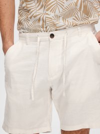 Shorts en lin blanc avec une taille élastiquée réglable et des poches à l'avant. Le tissu a une finition texturée, offrant une apparence légère.