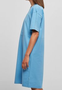 Sukienka z krótkim rękawem, wykonana z niebieskiej bawełny, o luźnym kroju, do kolan, z subtelnymi detalami na bocznych szwach. Gładka faktura, bez widocznych wzorów.