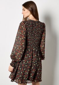 Kwiecista sukienka z czarnym tłem i czerwonymi oraz żółtymi kwiatami, z długimi bufiastymi rękawami, marszczoną talią i luźnym, warstwowym dołem.