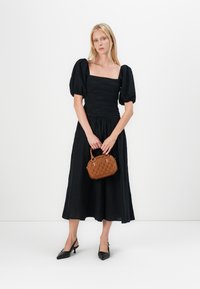Abito nero a maniche puff con scollatura quadrata e corpino arricciato, abbinato a una borsa marrone testurizzata e tacchi slingback neri.