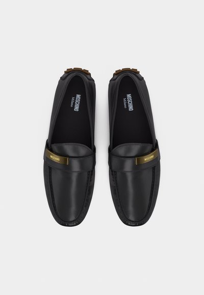 Paire de mocassins Moschino Milano en cuir noir avec plaques logo dorées sur les brides, vue de dessus sur fond blanc.