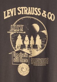 Hall halli puuvillane T-särk, millel on kreemjat värvi graafiline kujundus kauboi sõitmas, ringikujuline muster, tekst "Levi Strauss & Co" ja brändi logo.