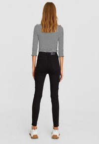 Pantalones cargo negros de corte ajustado, con bolsillos a los lados y en la parte trasera. Combinados con una camiseta de rayas gris y blanca de manga larga.