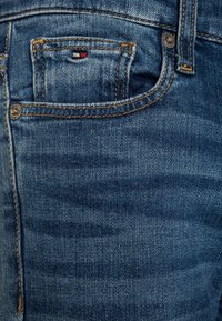 Denim jeans featuring a light blue color, classic five-pocket design, and visible stitching details with a small red, white, and blue logo.