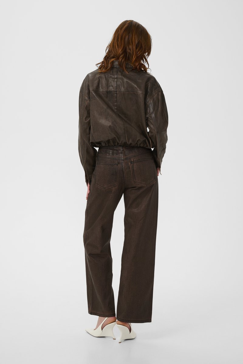 Brown leather jacket with a cropped design, paired with high-waisted, wide-leg brown jeans. White pointed heels complete the outfit.