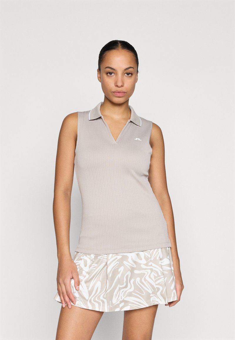 Top de polo sin mangas en beige con textura acanalada y cuello blanco, combinado con una falda corta ligera con un patrón que presenta diseños blancos ondulados.