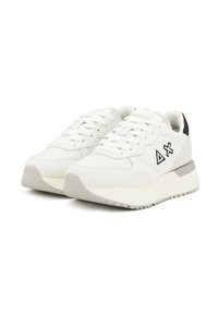 Un paio di sneaker bianche con simboli neri del logo sui lati, lacci bianchi, suole grigie e dettagli sul tallone a motivo nero su uno sfondo bianco.