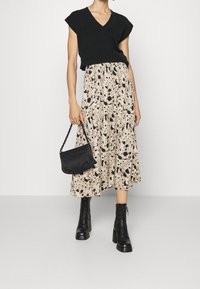 Svart kortärmad stickad topp, mönstrad plisserad midi kjol i beige med svarta accenter, svarta läderankelboots och en liten svart handväska.