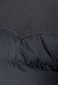 Dark gray puffer jacket featuring a quilted upper section, smooth lower section, and visible stitching. Material appears lightweight and water-resistant.