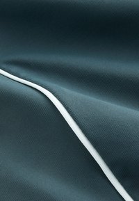 Gros plan d'un tissu bleu sarcelle foncé avec un tissage diagonal fin et un seul passepoil blanc lisse courant en diagonale.