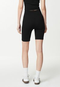 Shorts de vélo noirs côtelés avec une taille haute, un design ajusté et des ourlets bordés, associés à des baskets blanches et des chaussettes mi-mollet.