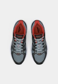 Sapatos atleticos cinzentos com detalhes pretos, forro vermelho, parte superior em malha para respirabilidade e solas de borracha brancas. Possui atacadores e marcação na língua.