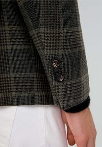 Manga de blazer de patrón de espiga en lana de color verde oscuro y marrón, con tres botones oscuros y un puño de punto texturizado.