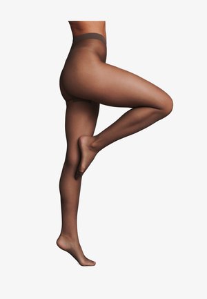 Gambe che indossano collant marroni trasparenti, una gamba piegata al ginocchio e sollevata, su sfondo bianco.