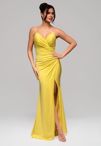 Robe de soirée jaune avec un design ajusté, décolleté en V profond, fronces à la taille et une fente haute sur la cuisse. Épaulettes à bretelles et texture douce.