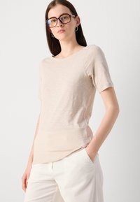 Beige lyhythihainen paita pehmeästä kankaasta, jossa on pyöreä kaula-aukko ja slim fit -leikkaus. Yhdistetty teksturoidun vaaleankerman värisiin housuihin.