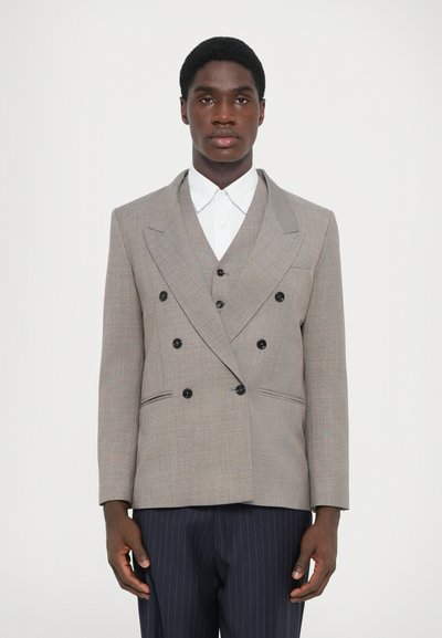 Grauer doppeltknöpfbarer Blazer mit schwarzen Knöpfen, Reverskragen und zwei Seitentaschen. Getragen über einem weißen Hemd mit Kragen und navyblauen Nadelstreifen-Hosen.