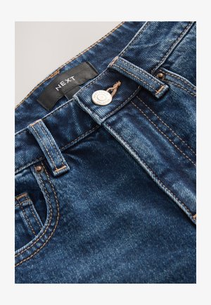 Donkere blauwe spijkerbroek met contraststiksels, knoopsluiting en een geweven label. Gladde textuur met lichte vervaging op sommige plekken.