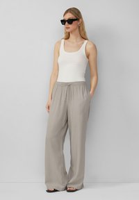 Grijze, wijde broek met een elastische tailleband en zakken, gecombineerd met een aansluitend wit tanktop. Zwarte zonnebril maakt de look compleet.