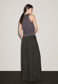 Gray sleeveless top with a fitted hem, paired with black striped wide-leg trousers, featuring a smooth texture and minimalist design.