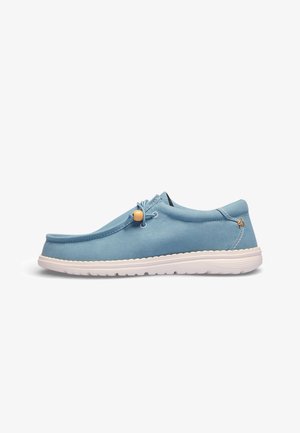 Zapato casual azul claro tipo slip-on con suela blanca y cordón ajustable con cuenta de madera, costuras laterales y corte bajo en el tobillo.