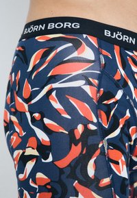 Moške spodnje hlače BJÖRN BORG z mornarsko modro podlago in barvitim abstraktnim vzorcem v rdeči, oranžni, beli in črni barvi. Mehka tkanina z elastičnim pasom.