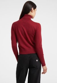 Maglione rosso a collo alto in un design aderente con dettagli a coste, abbinato a pantaloni neri a vita alta con un logo a triangolo sulla tasca posteriore.