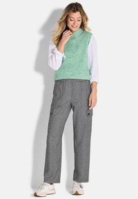 Mintgrüner gestrickter Weste über einem weißen Langarmshirt, kombiniert mit grauen Cargo-Hosen mit Seitentaschen und geradem Schnitt.