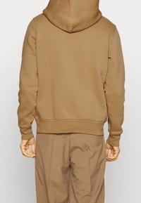 Brown hooded sweatshirt with a simple design, featuring a soft texture and ribbed cuffs and hem. The back shows a clean, seamless finish.