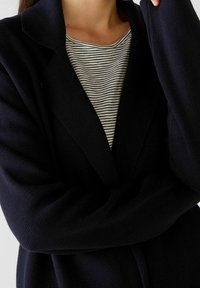 Marinblå stickad cardigan med texturerad yta, med en sjalkrage och öppen fram, lager på lager över en svart och vit randig topp.