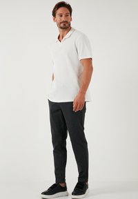 Bela kratka polo majica z rebrasto teksturo, kombinirana s temnosivimi zoženimi hlačami. Obutev ima črne akcentne detajle in eleganten dizajn.