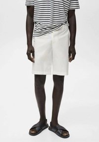 Vita bomullsshorts med en avslappnad passform, tillsammans med en marinblå och vit randig t-shirt. Svarta slidesandaler fulländar looken.