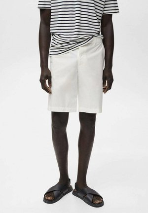 Shorts en coton blancs à coupe décontractée, associés à un t-shirt rayé bleu marine et blanc. Des sandales à glissière noires complètent le look.