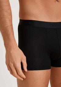 Boxer briefs neri in cotone con un elastico con logo, caratterizzati da una texture liscia e un design aderente, con una mano visibile sul lato.