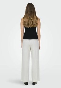Must mustriba tank top musta, millele on ühendatud laiad, heledast hallist kangast püksid, millel on sile tekstuur ja kerge cuffs.