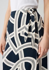 Jupe à motifs géométriques bleu marine et crème avec un détail de taille nouée. Le tissu est lisse avec des lignes et des formes contrastées tout au long.