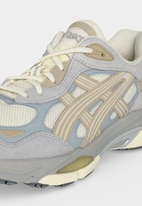 Αθλητικό παπούτσι σε μπεζ, ανοιχτό μπλε και λευκό με πάνελ από δίχτυ και σουέντ, κρεμ κορδόνια και λεπτομέρεια με μοτίβο στη σόλα.