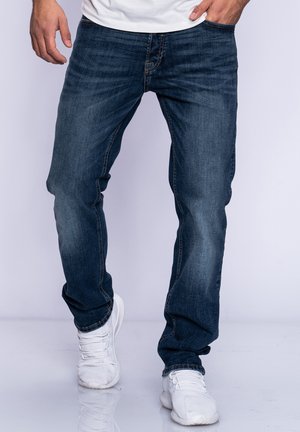 Dark blue denim jeans with a straight leg fit, featuring subtle fading and contrast stitching, paired with white athletic shoes.