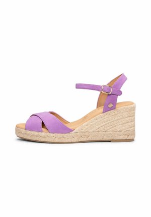 Sandalia cuña de ante morado con plataforma de yute trenzado, tira en el tobillo y detalle de hebilla pequeña dorada, mostrada sobre fondo blanco.